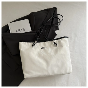 Detail view of cream tote bag with wrinkled texture, black rope strap and metal logo