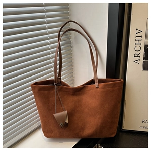 Detail of caramel suede tote bag featuring sleek shoulder straps and a triangle metal charm