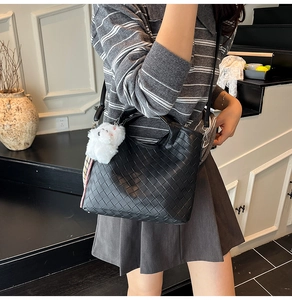Detail of black woven leather tote with white plush bunny charm and adjustable strap