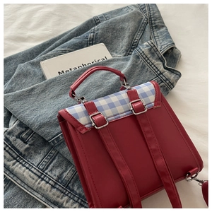 Détail du sac à dos en cuir mat rouge et tissu à carreaux bleus sur veste en jean