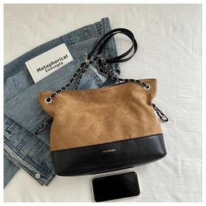 Detail of quilted brown suede and black leather tote bag with a golden chain strap