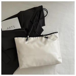 Detail of cream tote bag featuring black rope handles and elegant metal adjustment rings
