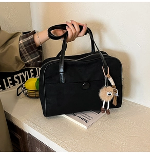 Detail of black tote bag with zipper and cute brown plush monster charm on textured surface
