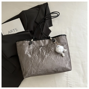 Close-up of metallic silver pleated tote bag with fine black straps and plush charm