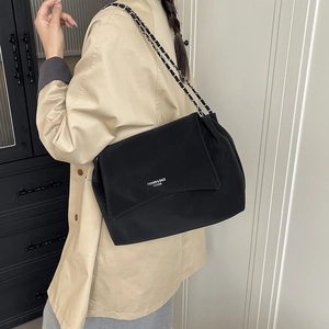 Retro black leather shoulder bag with metal chain strap worn on a light trench coat