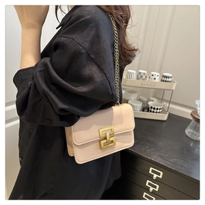 Detail of light beige crossbody bag with gold lock and chain strap worn by a model
