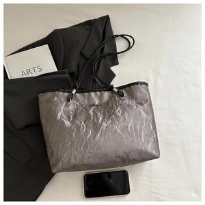 Overhead view of silver tote bag with crinkled texture, black straps and ARTS book