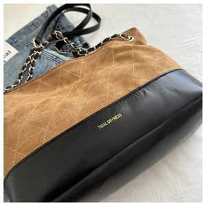Detail of quilted brown suede tote with gold chain strap and brand lettering