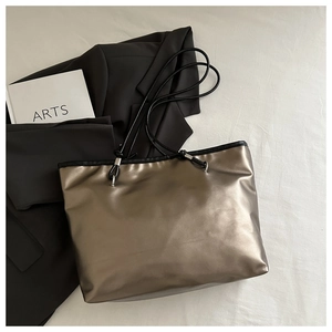 Close-up of metallic bronze tote bag with slim black handles on minimalist background