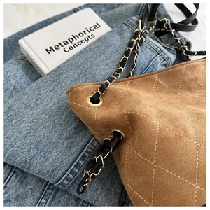 Detail of brown suede bucket bag with quilted diamond pattern and gold chain strap