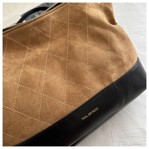 Detail of quilted suede tote bag featuring contrast leather trim and gold brand logo