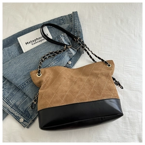Detail of vintage quilted bucket bag with beige suede, black leather, and gold chain strap