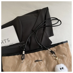 Detail view of khaki pleated texture tote bag with black straps and plush pendant