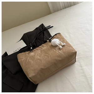 Detail of khaki pleated tote bag with dark brown base and white fur ball charm accessory