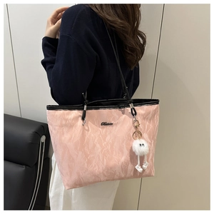 Detail of pink tote bag with crinkled texture, black straps, and plush pendant