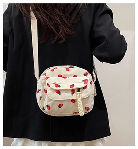 Detail of beige corduroy crossbody bag with strawberry print and woven white strap