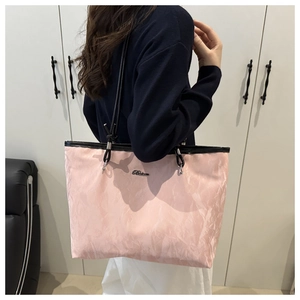 Detail of pink tote bag with pleated texture and black straps shown on shoulder