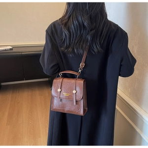 Brown vintage faux leather backpack with top handle and golden buckle details shown on model