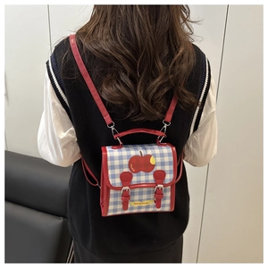 Détail d'un sac à dos à carreaux rouges et bleus avec motif pomme et broderie NCTU chic