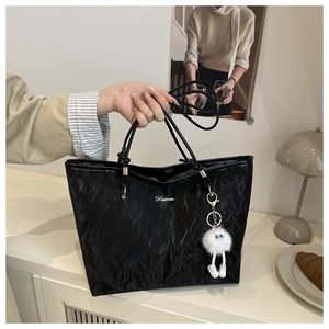 Close-up of black textured tote bag with silver logo and a white fluffy doll keychain