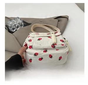 Detail showing white corduroy fabric with red strawberry print and woven zipper pull