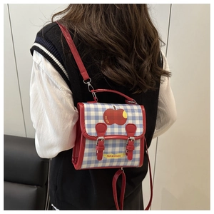 Detail of red and blue plaid backpack with apple pattern and dual buckle strap design