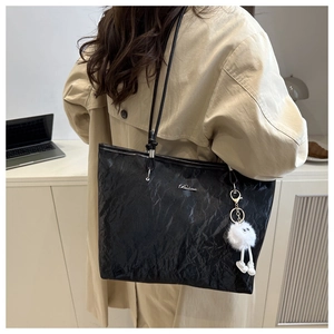 Detail of a black large tote bag with pleated texture and a cute charm for work commute