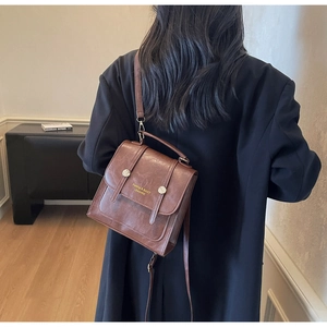 Detailed back view of vintage brown leather backpack worn with a black wool coat