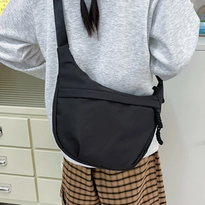 Minimalist black nylon crescent crossbody bag with wide strap worn by a female model
