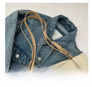 Detail of off-white quilted tote bag with thin brown handles on a blue denim jacket