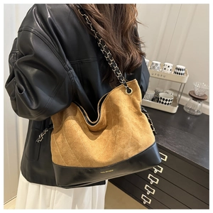 Detail of a large quilted tote bag with chain strap worn by a model in a cozy cafe