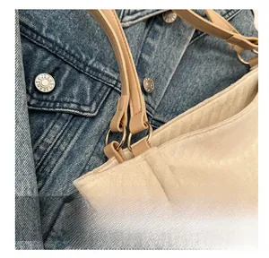 Detail of metal ring hardware and leather strap on a beige textured fabric tote bag