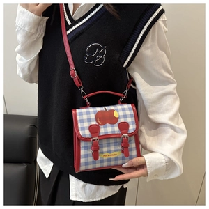 Détail du sac à bandoulière à carreaux bleus avec écusson pomme rouge et cuir rouge