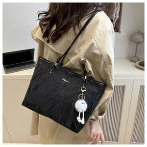 Close-up of black glossy tote bag with metal logo and cute white plush doll pendant