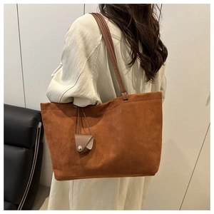 Brown suede tote bag with leather strap and triangle charm shown on model's shoulder