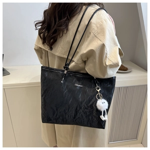 Detail of black pleated tote bag with silver logo and white plush charm on model's shoulder