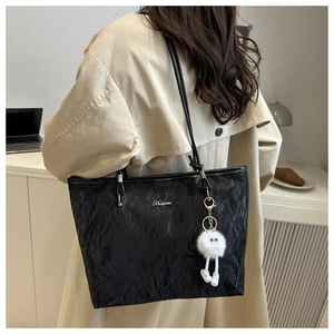 Detail of black tote bag with wrinkled texture, metal logo and plush pendant accessory
