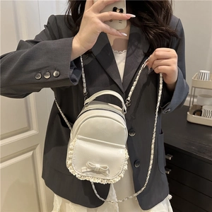 Detailansicht der weißen Mini-Tasche mit Spitze und Schleife auf grauem Anzug