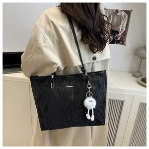 Detail of black tote bag featuring textured crinkled leather and white plush doll charm