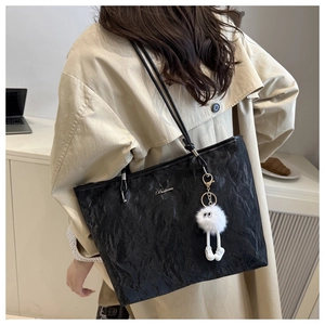 Close-up of black pleated tote bag featuring silver metal logo and a cute plush charm