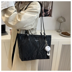 Detail of black tote bag with unique pleated texture and a cute plush ball keychain