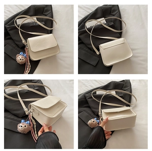 Détail d'un sac bandoulière crème avec gaufrage dessin animé et pendentif ours en peluche
