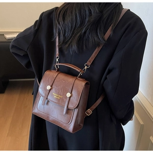 Close-up of a brown vintage faux leather backpack with gold lettering and metal buckles