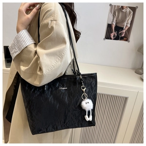 Detail of black pleated tote bag with silver Batena logo and plush charm accessory