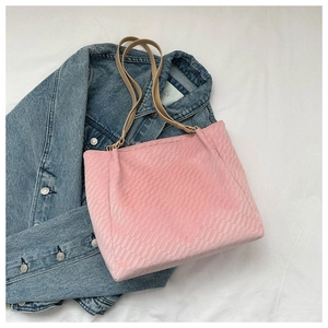 Pink woven tote bag with brown leather straps shown on blue denim background