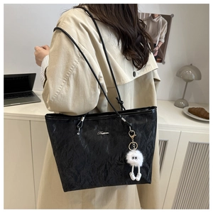 Close-up of black tote bag featuring glossy wrinkled texture and white plush charm