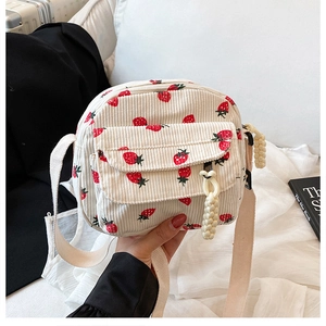 Detailed texture of off-white corduroy crossbody bag with vibrant red strawberry patterns
