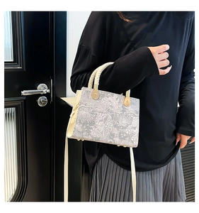 Detail of silver-grey floral jacquard crossbody bag with woven handle and gold hardware