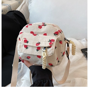Close-up of corduroy crossbody bag with strawberry embroidery and woven rope zipper pull
