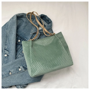 Detailed view of green quilted tote bag with brown faux leather straps on denim background